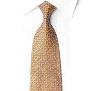 Golden-orange San-Dee rhinestone silk necktie knotted against a white shirt, showing blue-violet geometric loops and silver sparkles.